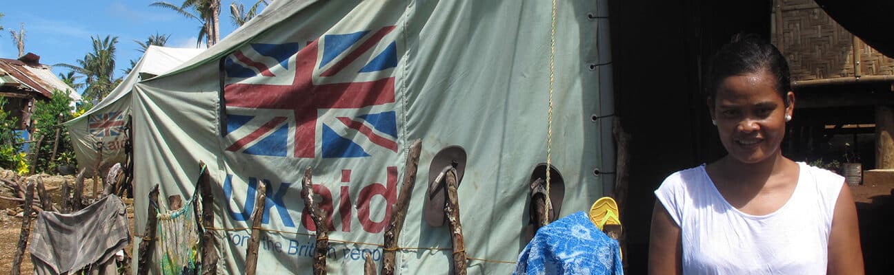 A woman stands in front of a tent supplied by UK aid, Philippines