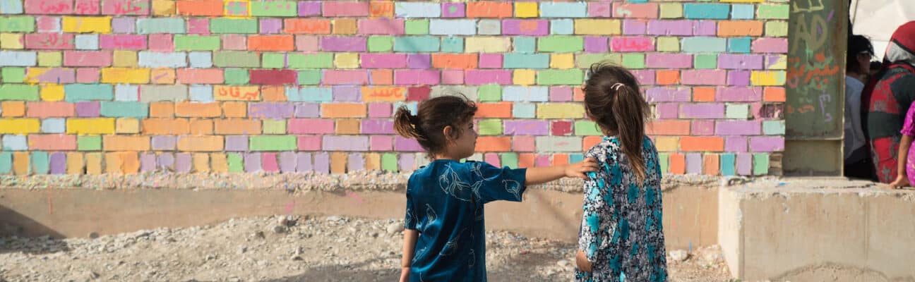 Children painting a wall mural with EU flag in Arbat camp, Iraq