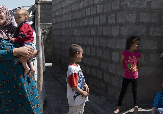 A Syrian-Kurdish woman and several children stand outside a home in Darashakran refugee camp in Iraqi Kurdistan