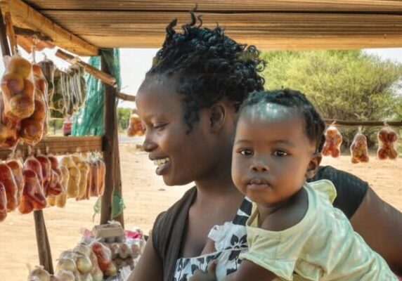 African street vendor, mother holding her child between the bags of tomatoes and cabbage