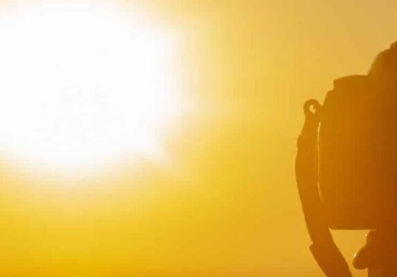 Silhouette of digital camera on a tripod in front of setting sun with orange sky.