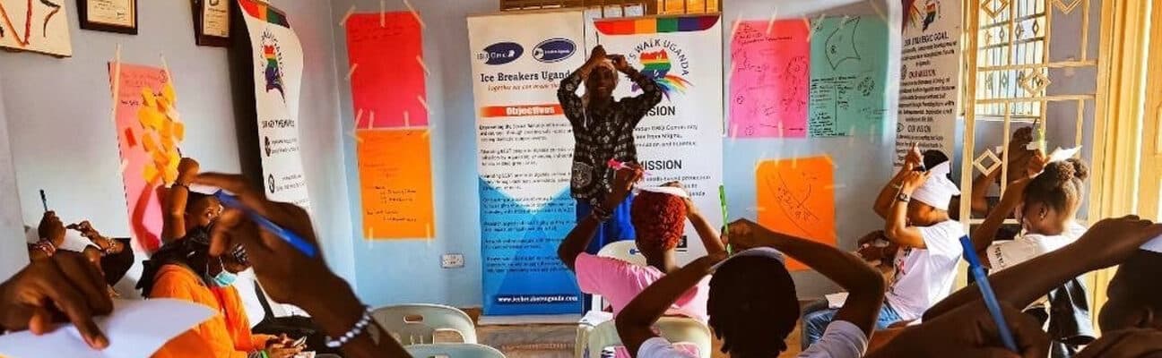 Classroom of students facing their teacher drawing on a sheet of paper on top of their heads. Credit: Let's Walk Uganda