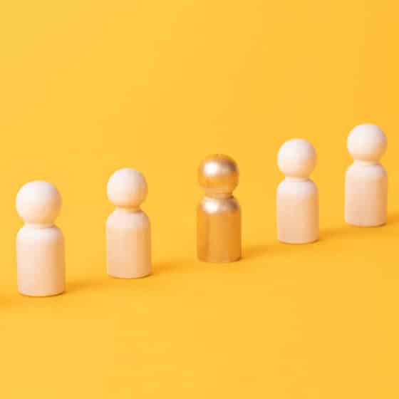 Row of wooden figurines with one gold figurine on yellow background