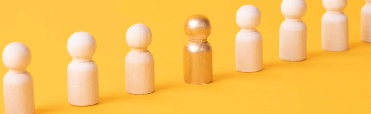 Row of wooden figurines with one gold figurine on yellow background