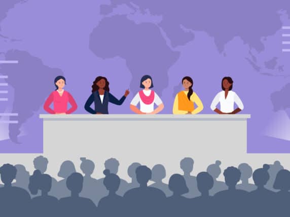 Multiethnic women sitting at the desk on stage and speak to an audience.