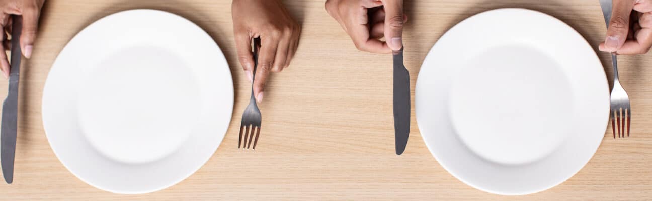 Two people hold cutlery near empty plates on table