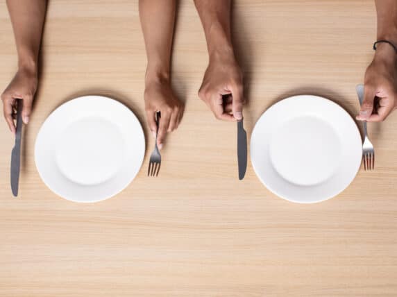 Two people hold cutlery near empty plates on table.