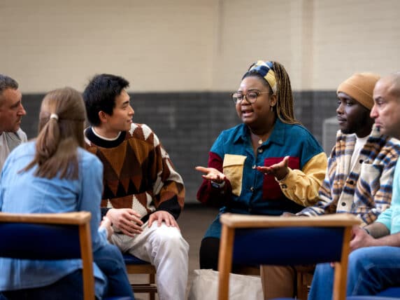 Group of adults sitting on chairs talking to each other.