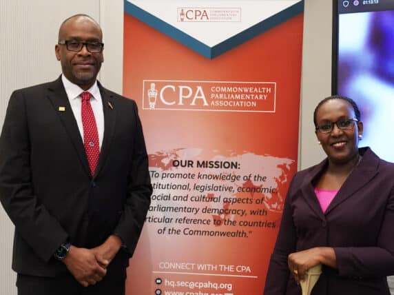 Commonwealth Parliamentary Association colleagues stand next to red banner of mission statement.