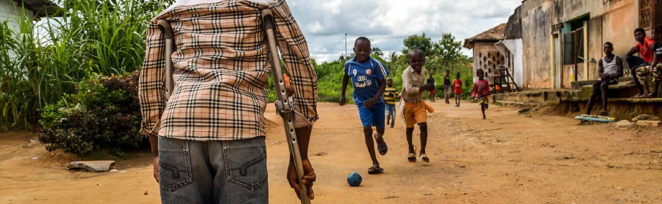 A child, Zambo, who has a physical impairment, watches his friends play at a Sightsavers supported inclusive school in Cameroon.