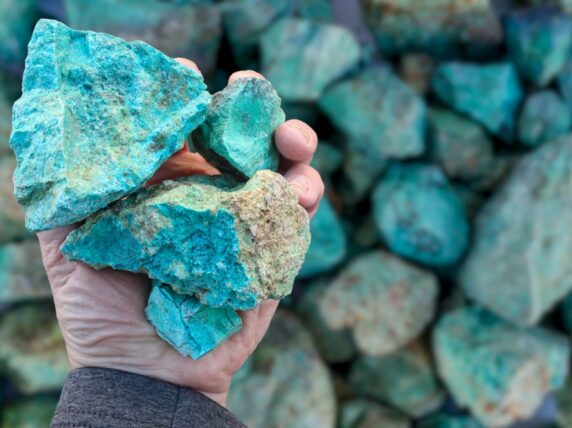 Blue green copper (Cu) oxide ore, held in hand, against background of ore that is out of focus. Mining.