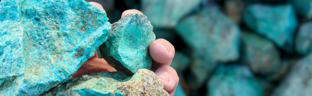 Blue green copper (Cu) oxide ore, held in hand, against background of ore that is out of focus. Mining.